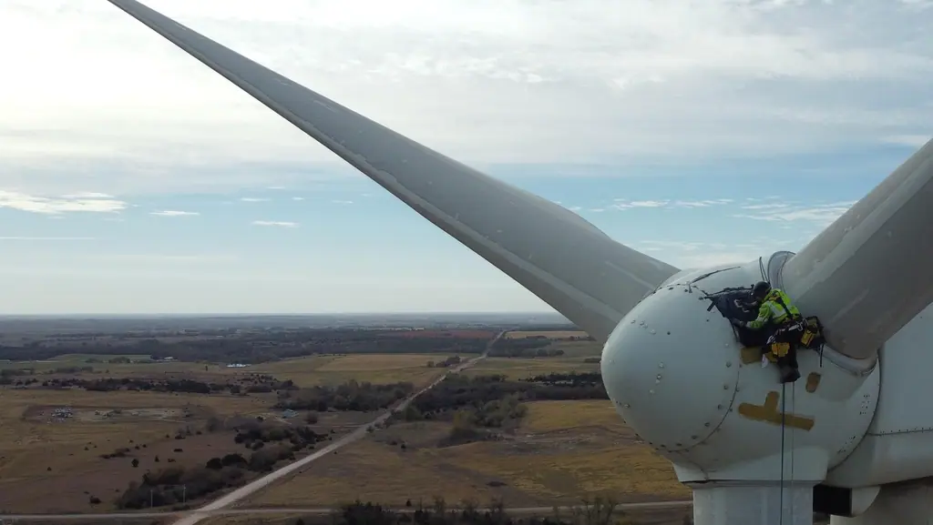 Rope access technician working at the hub of a wind turbine, high above open countryside